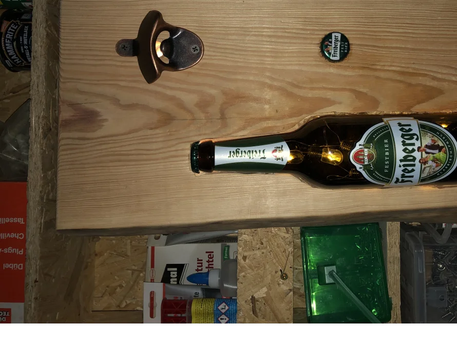 Ein Flaschenöffner und eine leere Glasflasche in einem Holzbrett.