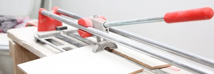 Ein Fliesenschneider mit einer Fliese und einem roten Griff.