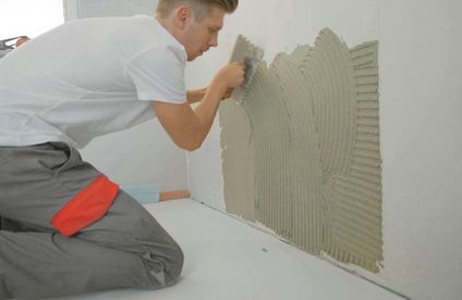 Wände fliesen: Fliesenkleber auftragen Mit einer Kelle bringt ein Handwerker Fliesenkleber an der Wand an.