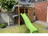 Ein Holzturm mit Rutsche und Kletterwand im Garten.