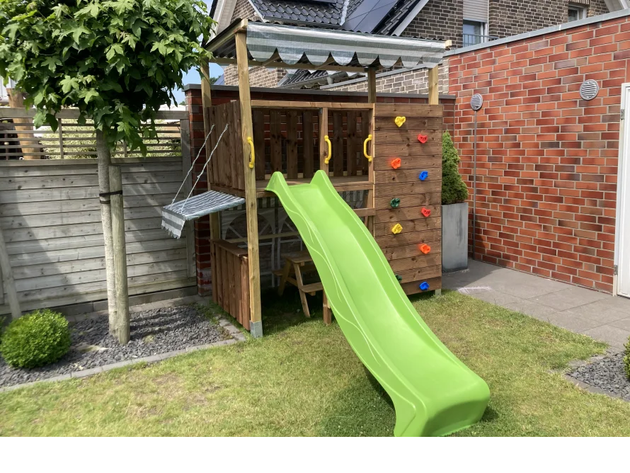 Ein Holzturm mit Rutsche und Kletterwand im Garten.