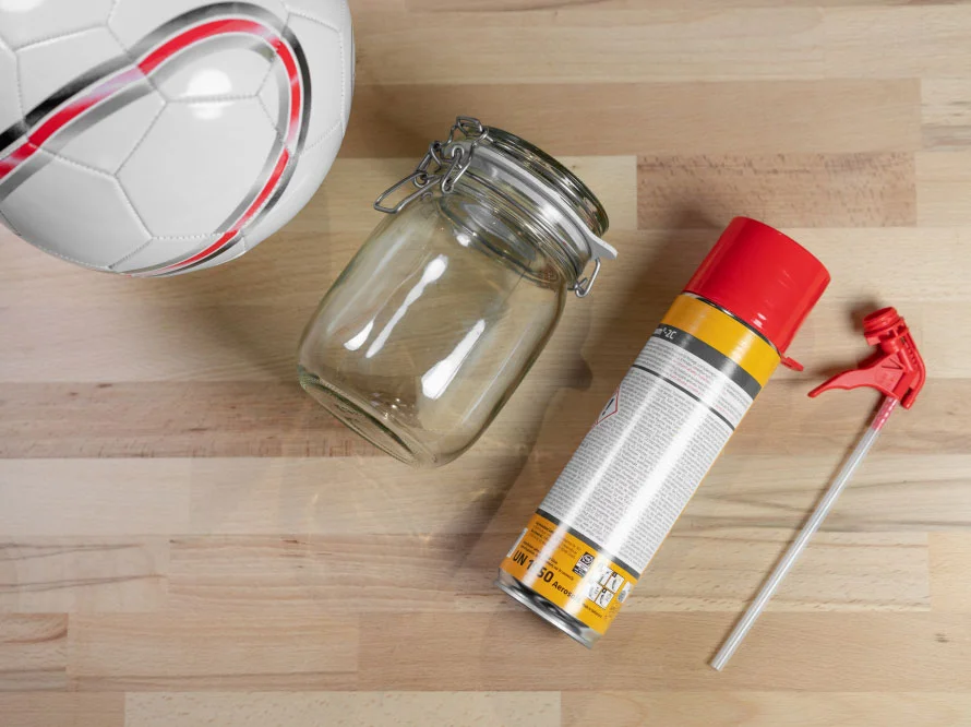 Ein Fußball, ein Einmachglas und eine Sprühflasche auf einem Holztisch