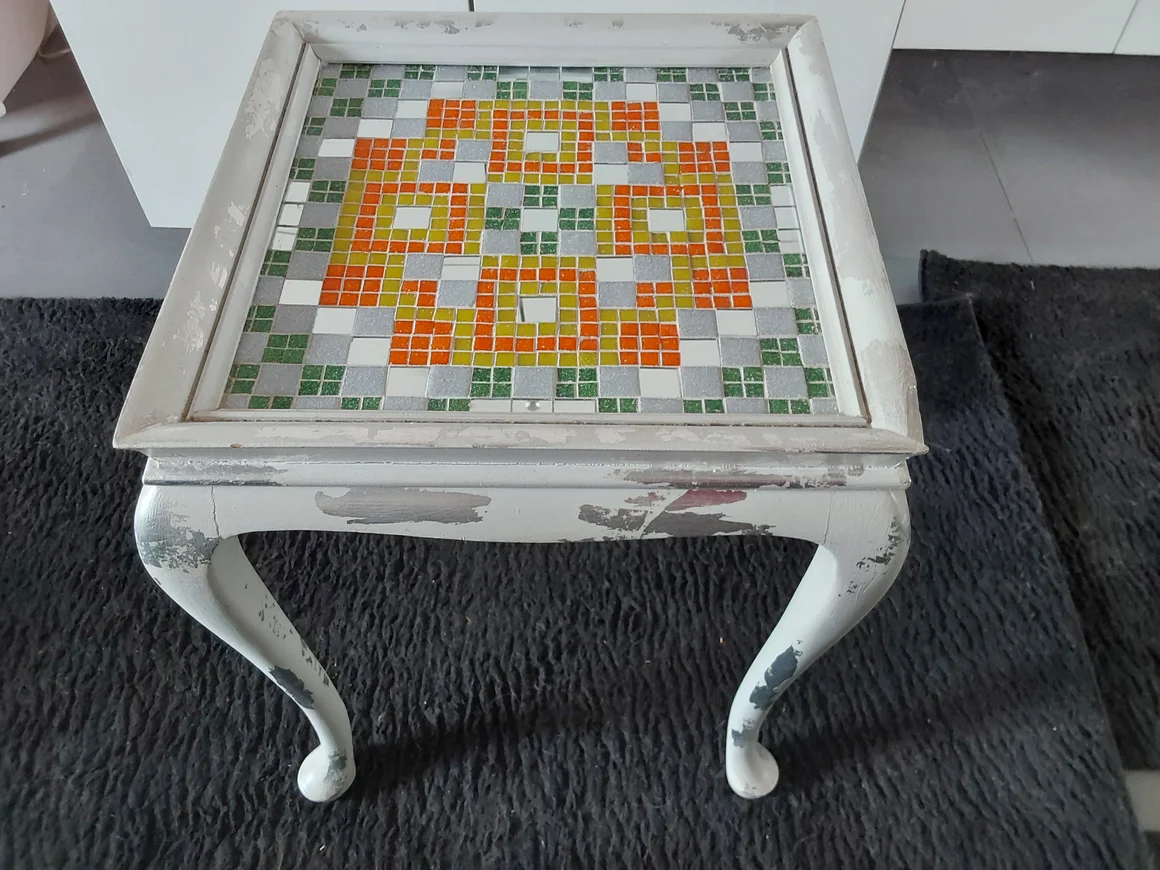 Abgenutzter weißer Tisch mit einer Mosaikplatte.