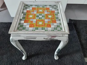 Abgenutzter weißer Tisch mit einer Mosaikplatte.