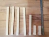 Sechs Holzlatten unterschiedlicher Länge liegen auf einer Holzarbeitsplatte. Rechts daneben liegt ein weißes Metall-Zollstock.