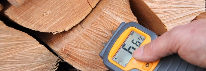 Eine Person misst mit einem Gerät die Feuchtigkeit von gestapeltem Brennholz.
