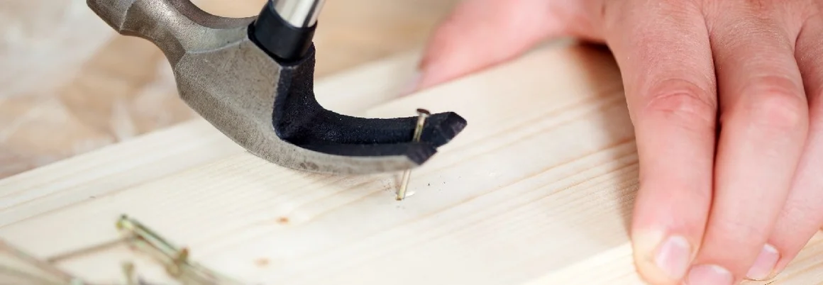 Hand hämmert einen Nagel in Holz