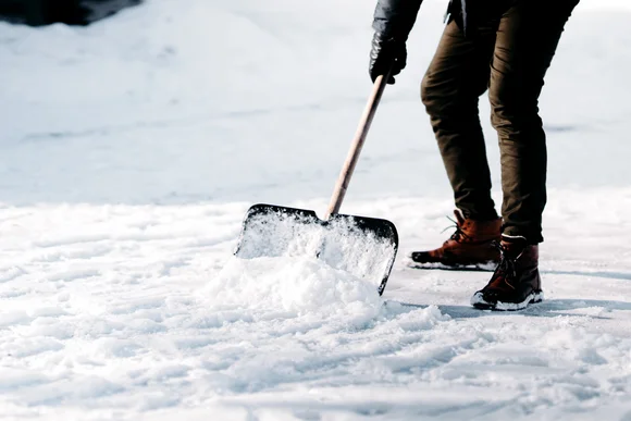 Person räumt Schnee mit Schneeschieber