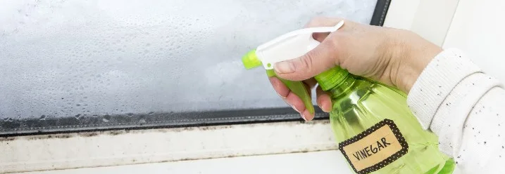 Hand sprüht mit Sprühflasche auf beschlagenes Fenster