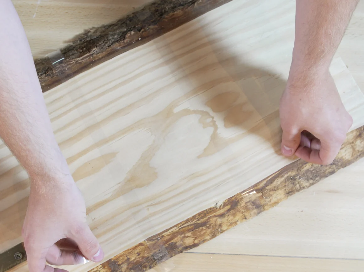 Person klebt Holzbrett mit Klebeband ab