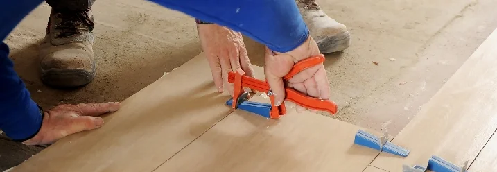 Person verlegt Fliesen mit einer Zange.