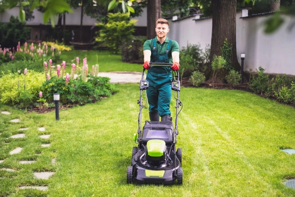 Eine Person mäht den Rasen mit einem Rasenmäher.