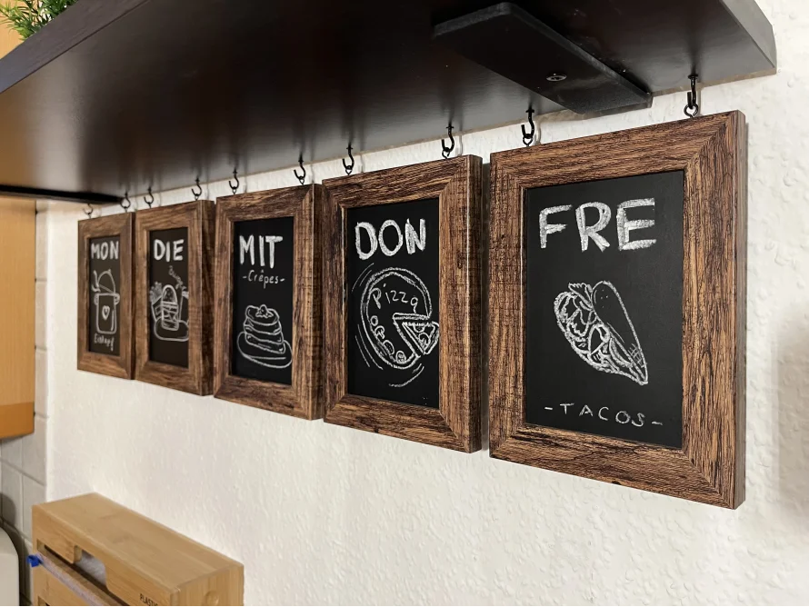 Kreativer Wochen-Speiseplan auf fünf hängenden, gerahmten Kreidetafeln.