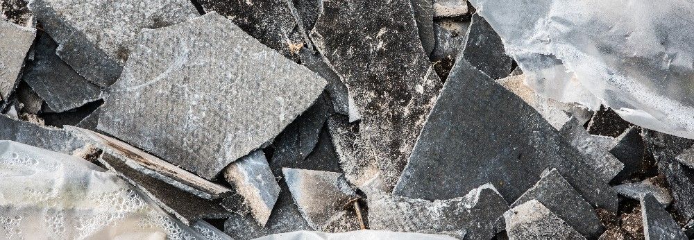 Entfernte Asbestplatten liegen auf einem Schutthaufen.