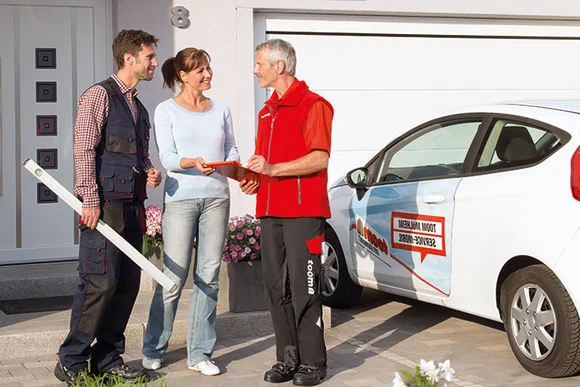 Drei Personen vor einem Haus, eine Person hält eine Wasserwaage.