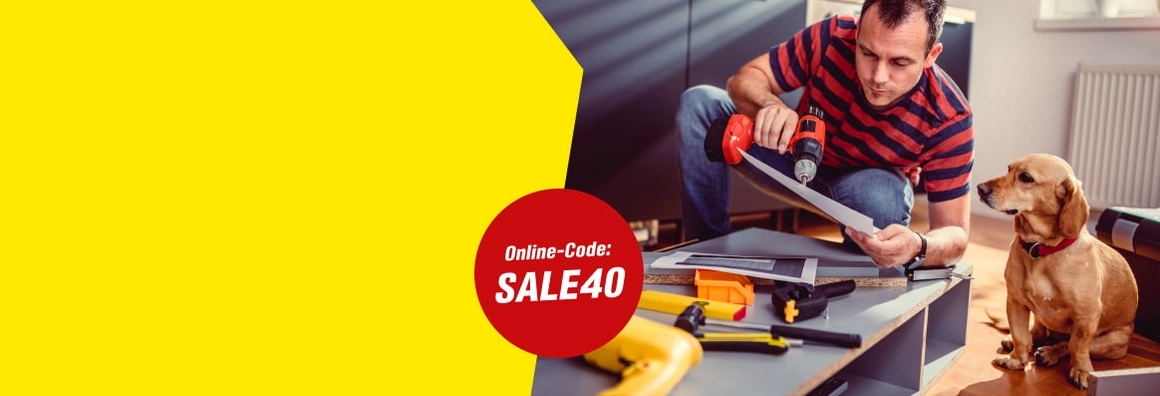 SALE40- Eine Person baut mit einem Akkuschrauber ein Möbelstück auf, daneben sitzt ein Hund.
