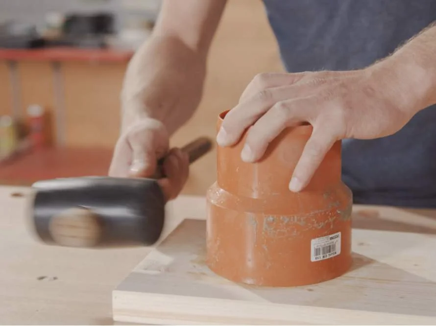 Person hämmert Rohr auf Holz