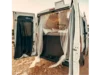Ein umgebauter Transporter mit geöffneten Hintertüren, die ein Bett im Inneren zeigen.