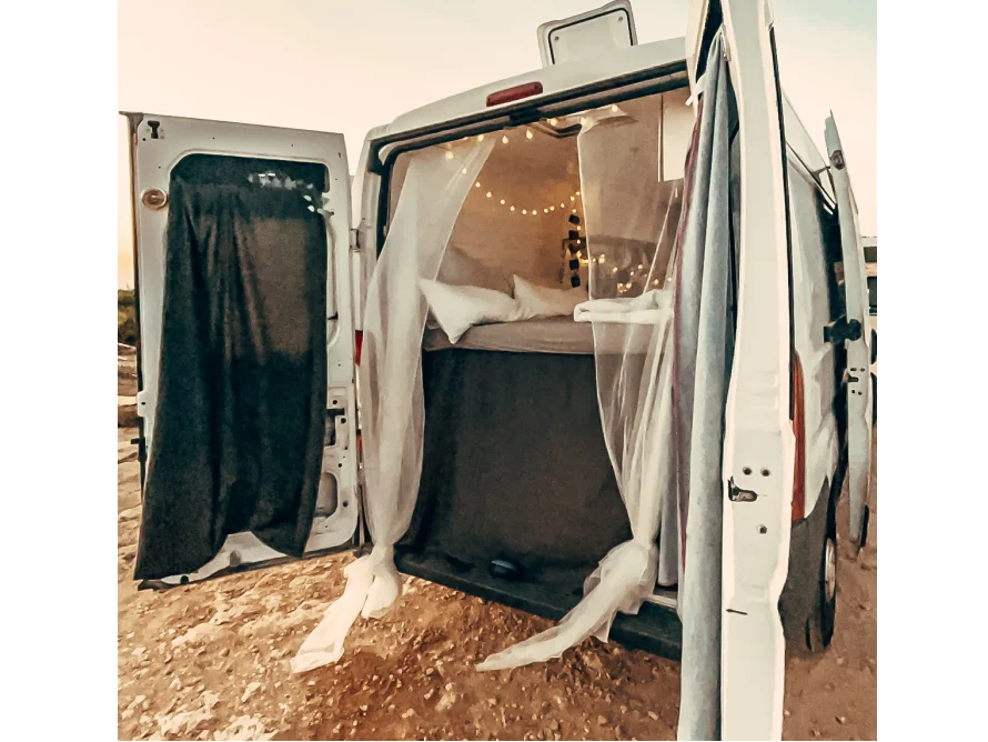 Ein umgebauter Transporter mit geöffneten Hintertüren, die ein Bett im Inneren zeigen.