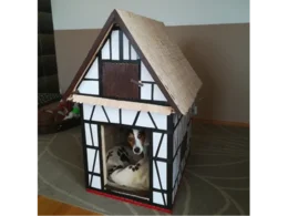 Ein Hund schaut aus einer Hundehütte in Form eines Fachwerkhauses