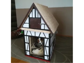 Ein Hund schaut aus einer Hundehütte in Form eines Fachwerkhauses