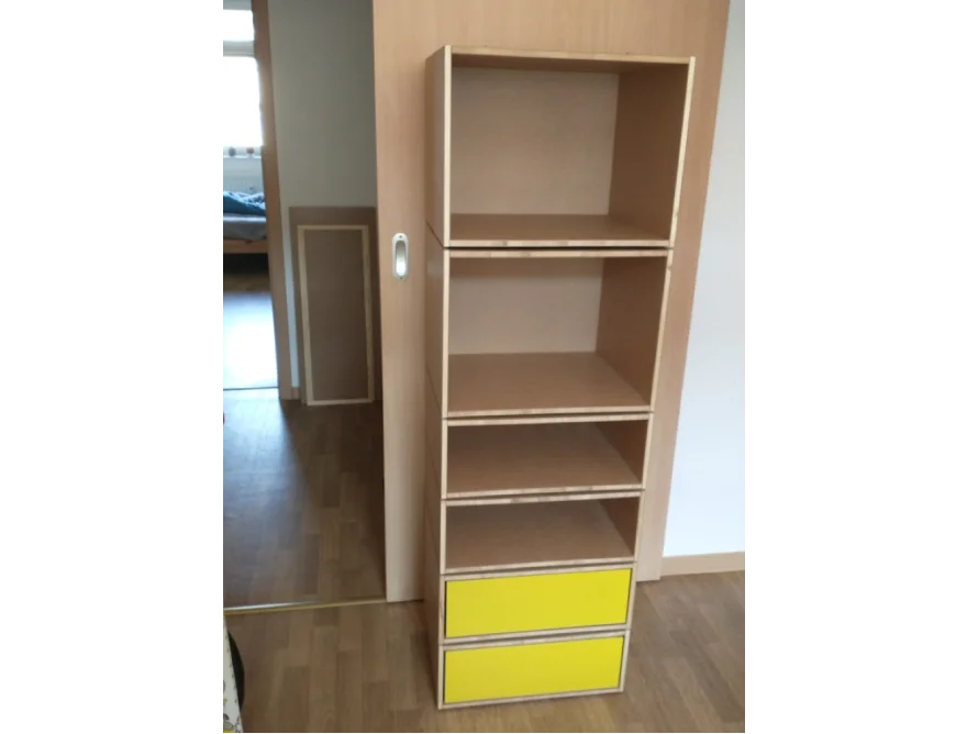 Schmales Regal aus Holz mit offenen Fächern und zwei gelben Schubladen.