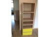 Schmales Regal aus Holz mit offenen Fächern und zwei gelben Schubladen.