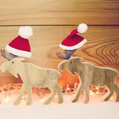 Zwei Holz-Elche mit Weihnachtsmützen im Schnee