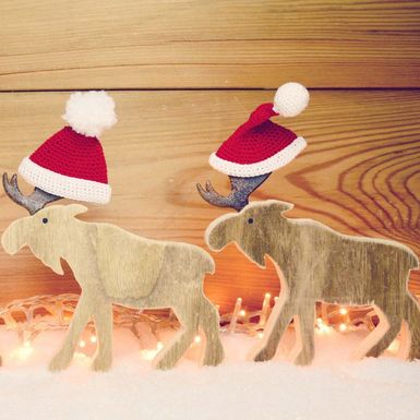 Zwei Holz-Elche mit Weihnachtsmützen im Schnee