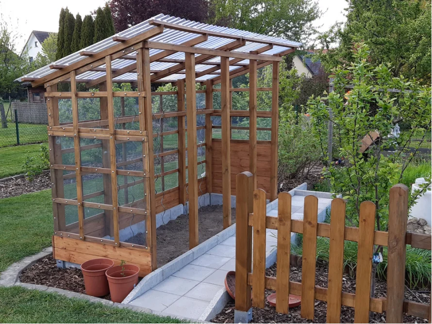 Kleines Gewächshaus aus Holz mit durchsichtigem Dach.