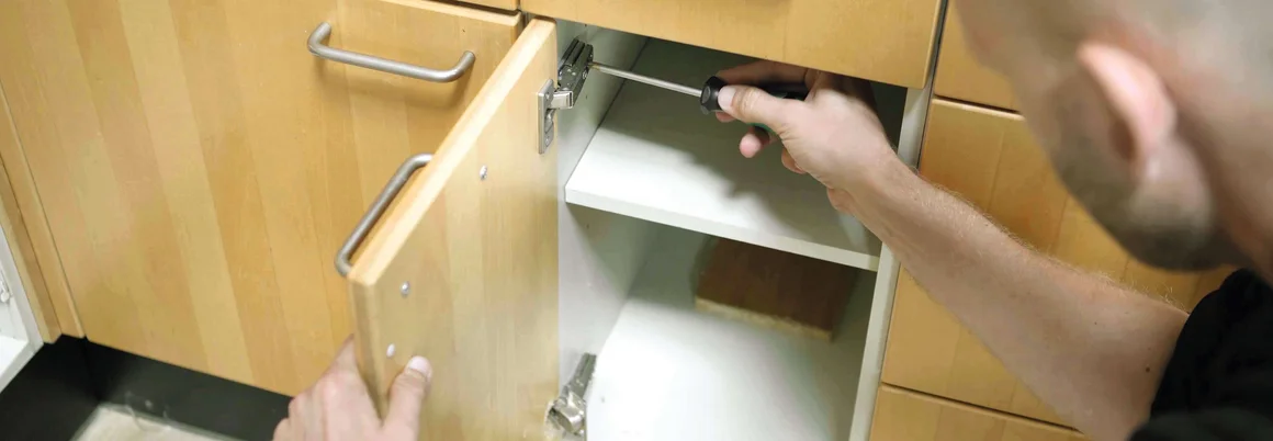 Person repariert Schrankscharnier mit Schraubenzieher.