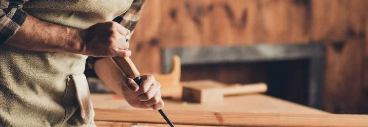 Person bearbeitet Holz mit Stechbeitel.