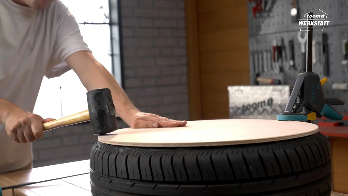 Person befestigt Holzplatte mit Hammer an Reifen