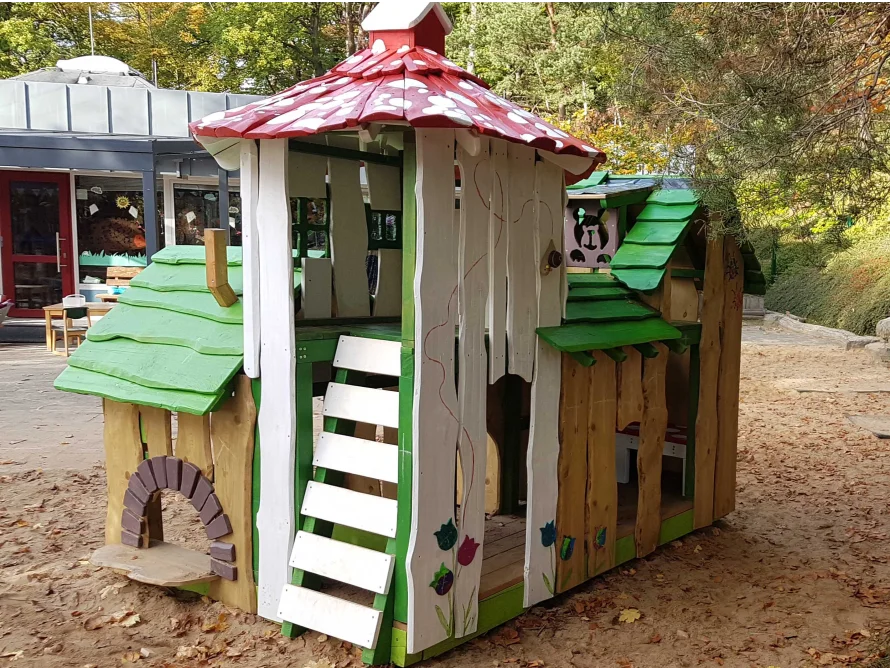 Hölzernes Spielhaus mit Pilzdach auf einem Spielplatz