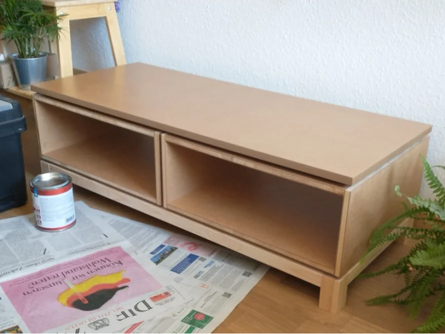 Ein TV-Lowboard aus Holz wird renoviert, daneben eine offene Farbdose.