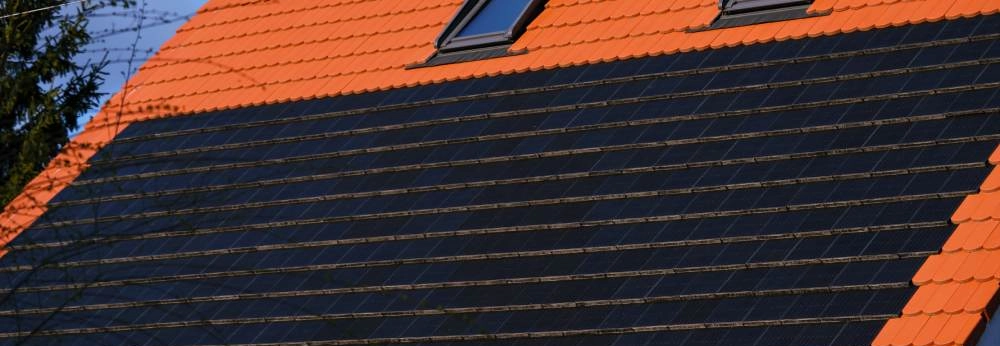 Rotes Ziegeldach mit schwarzen Solarmodulen und zwei Dachfenstern.
