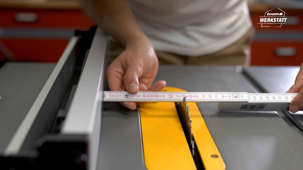 Person misst Abstand an Tischkreissäge mit Zollstock aus.