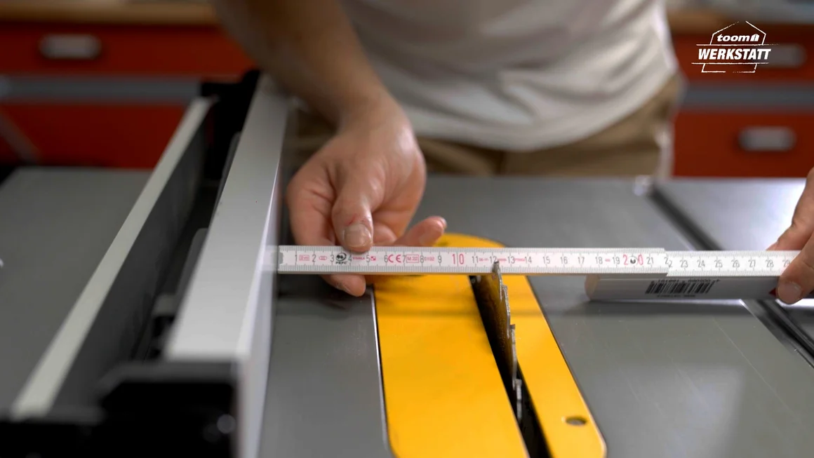 Person misst Abstand an Tischkreissäge mit Zollstock aus.