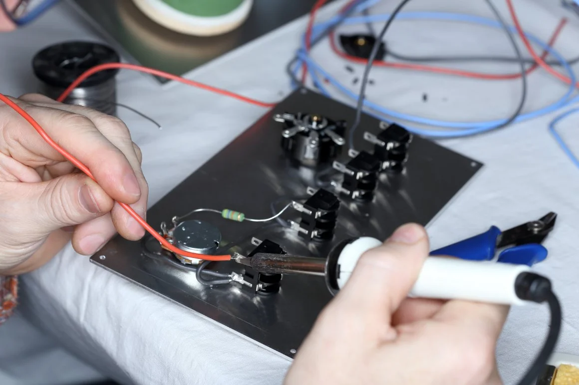 Eine Person arbeitet mit einem Lötkolben an elektronischen Bauteilen.