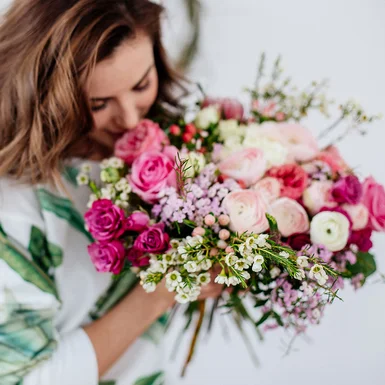 Person riecht an einem bunten Blumenstrauß