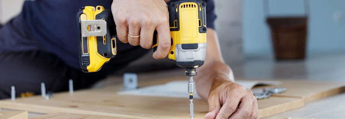 Person baut Holzmöbel mit Akkuschrauber zusammen