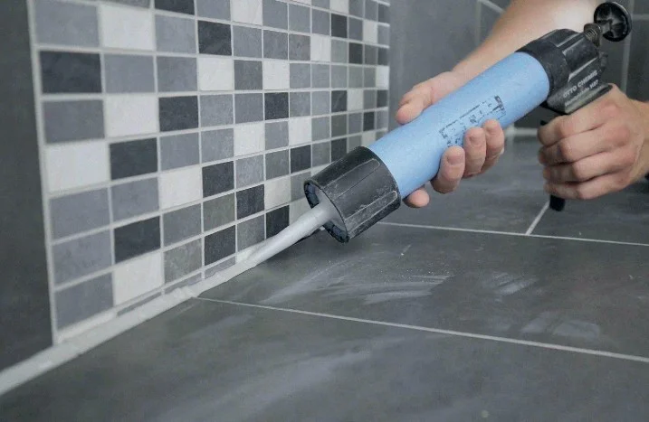 Person verfugt Fliesen mit Silikonpistole.