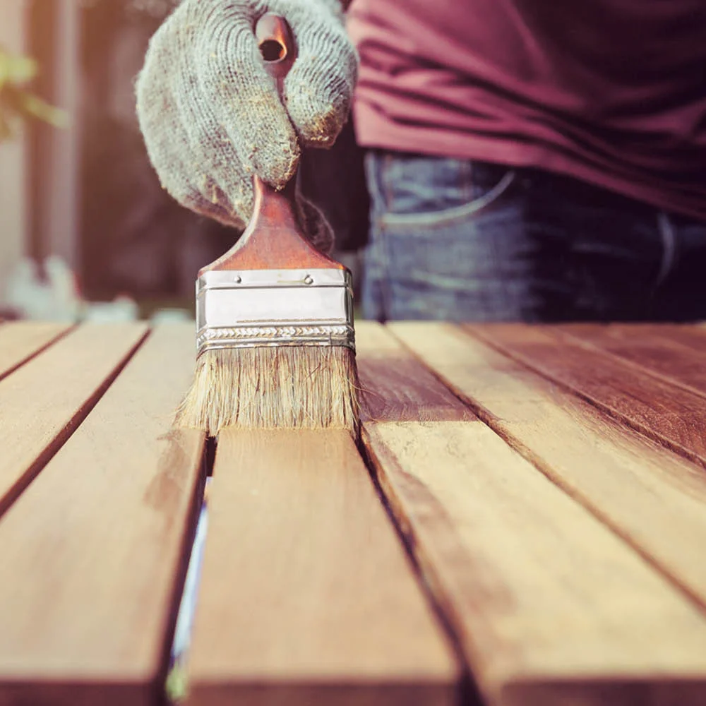 Person streicht Holz mit Pinsel.