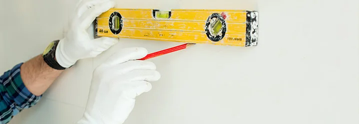 Eine Person zeichnet mit Wasserwaage und Stift eine Linie an die Wand.