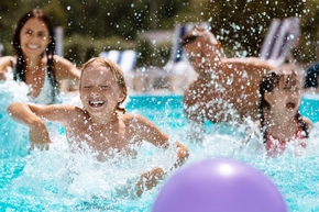 Ein lachendes Kind planscht mit seiner Familie im Pool.