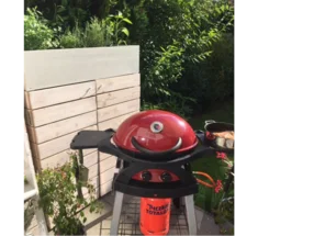Roter Gasgrill auf Terrasse vor Gartenhaus