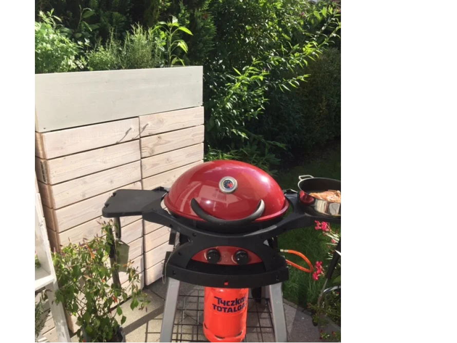 Roter Gasgrill auf Terrasse vor Gartenhaus