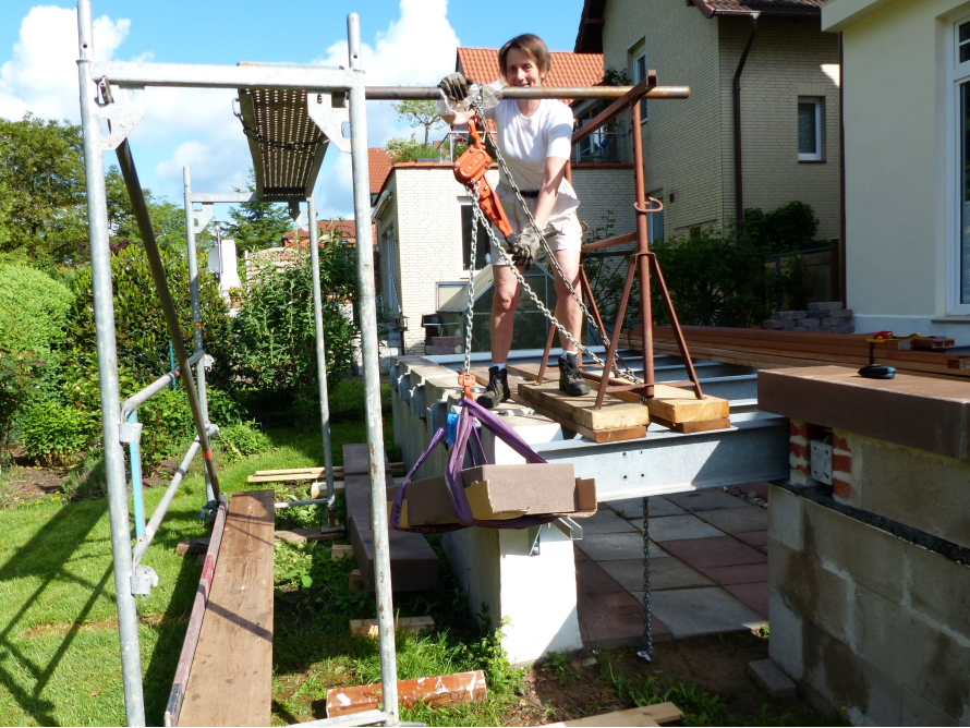 Person hebt mit Flaschenzug Material auf Gerüst