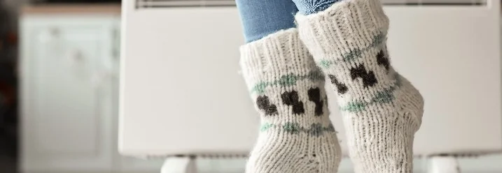 Person mit Wollsocken vor Heizkörper