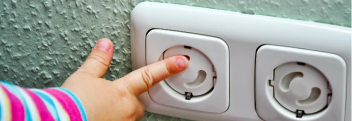 Kind zeigt auf Kindersicherung an Steckdose